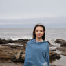 Woman wearing a blue poncho with floral patterns standing on a rocky beach.