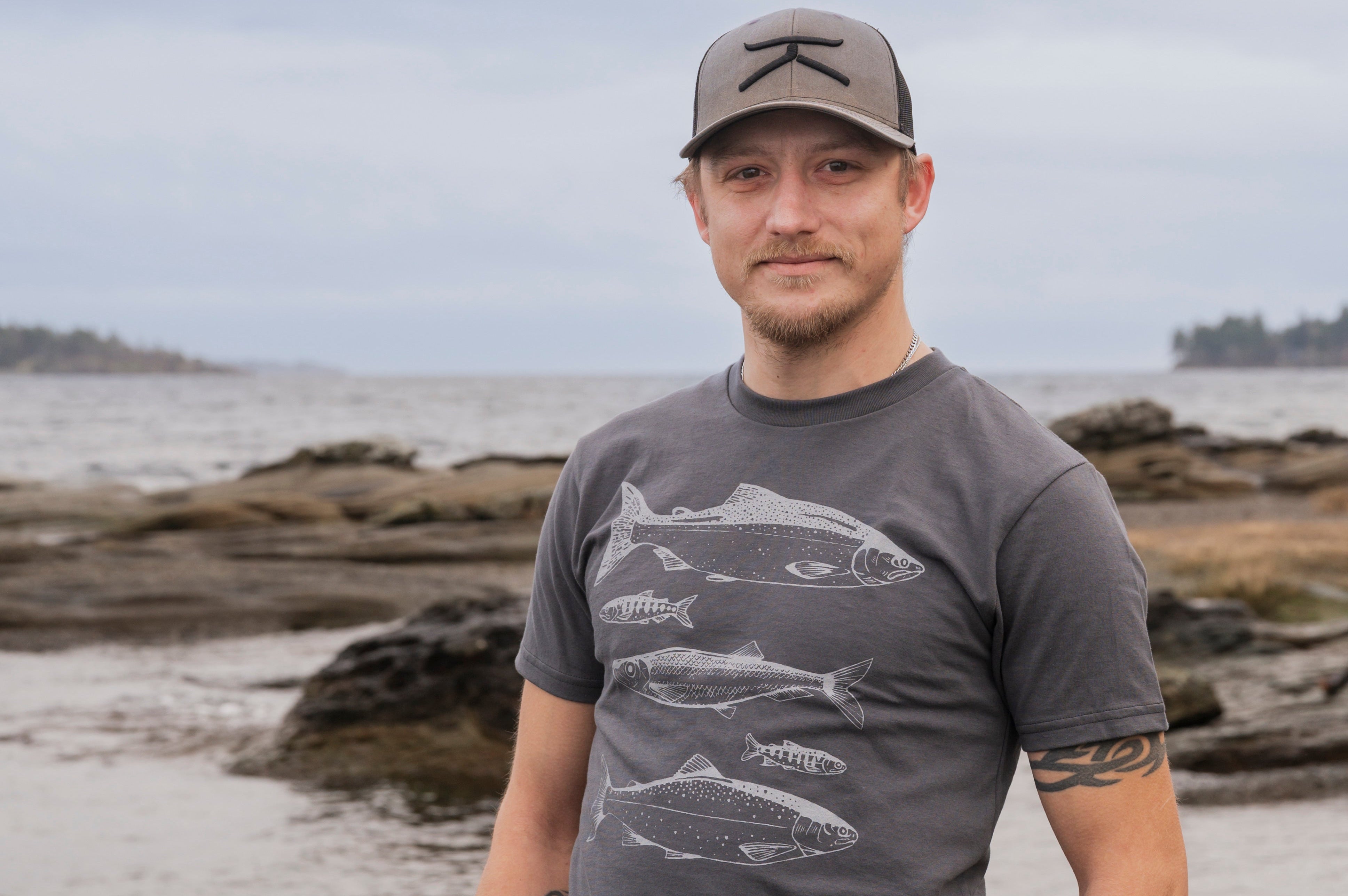 Man wearing a gray t-shirt with fish design on a beach