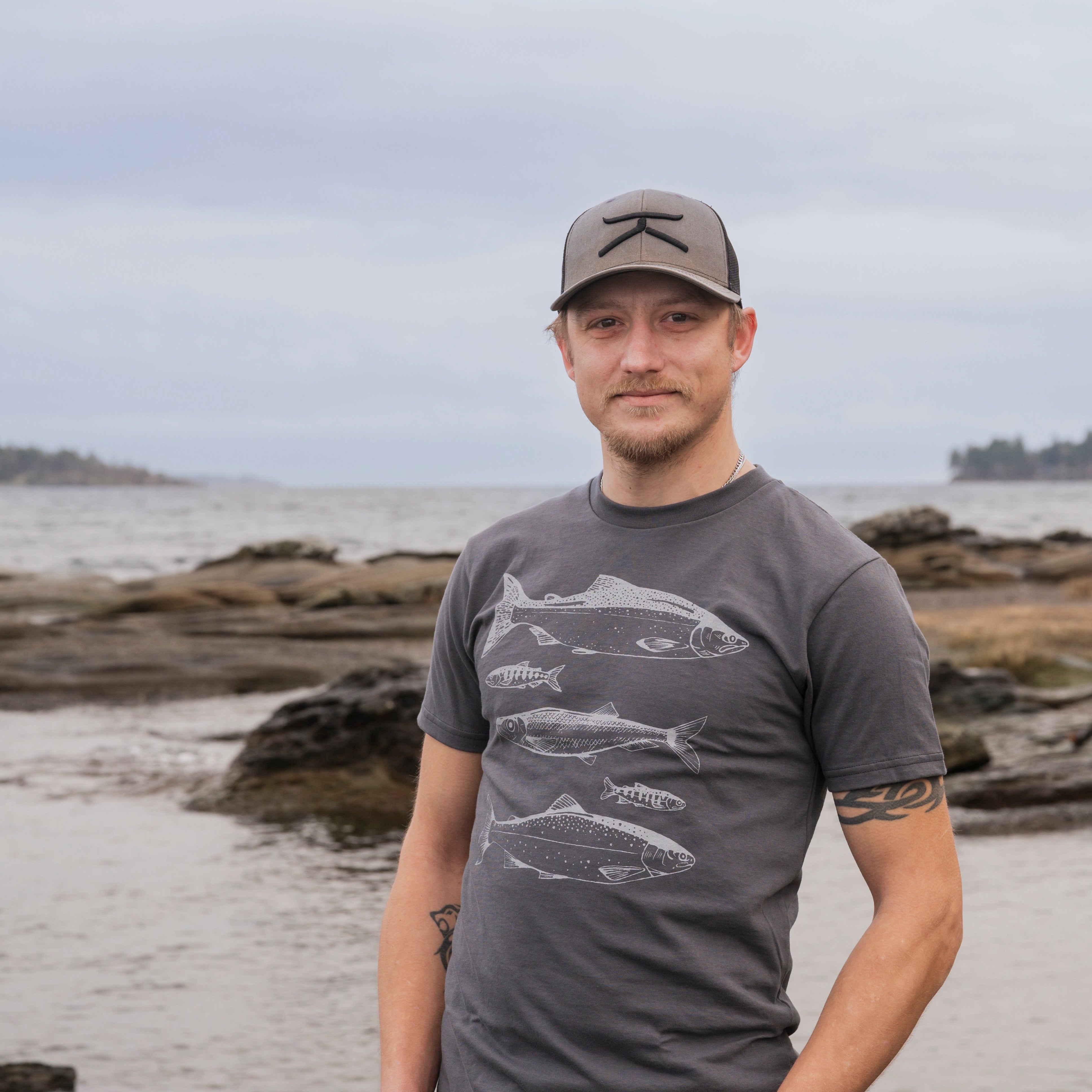 Man wearing a gray t-shirt with fish design on a beach