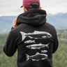 Person wearing a black hoodie with fish designs on the back, standing in a scenic outdoor setting.