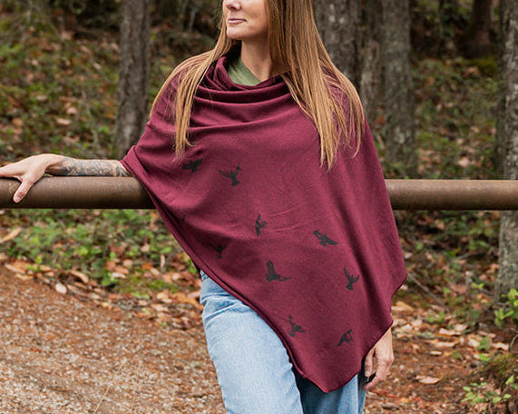 Woman wearing a burgundy poncho with black patterns in a forest setting