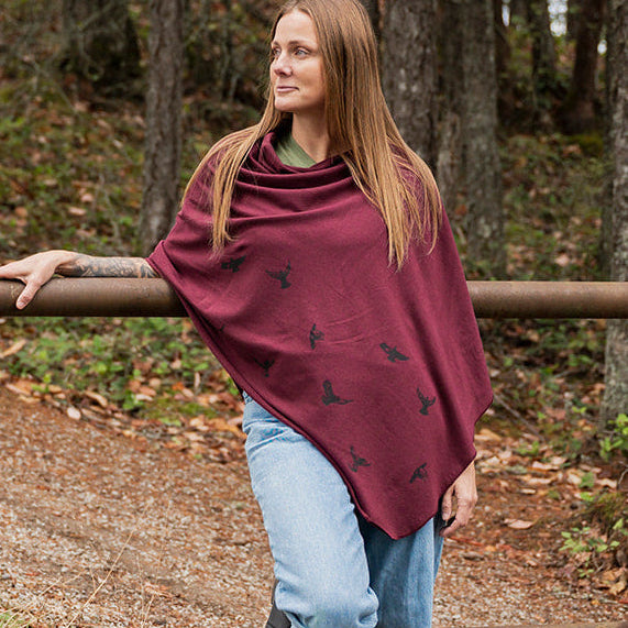 Woman wearing a burgundy poncho with black patterns in a forest setting
