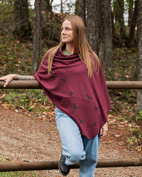 Woman wearing a burgundy poncho with black patterns in a forest setting