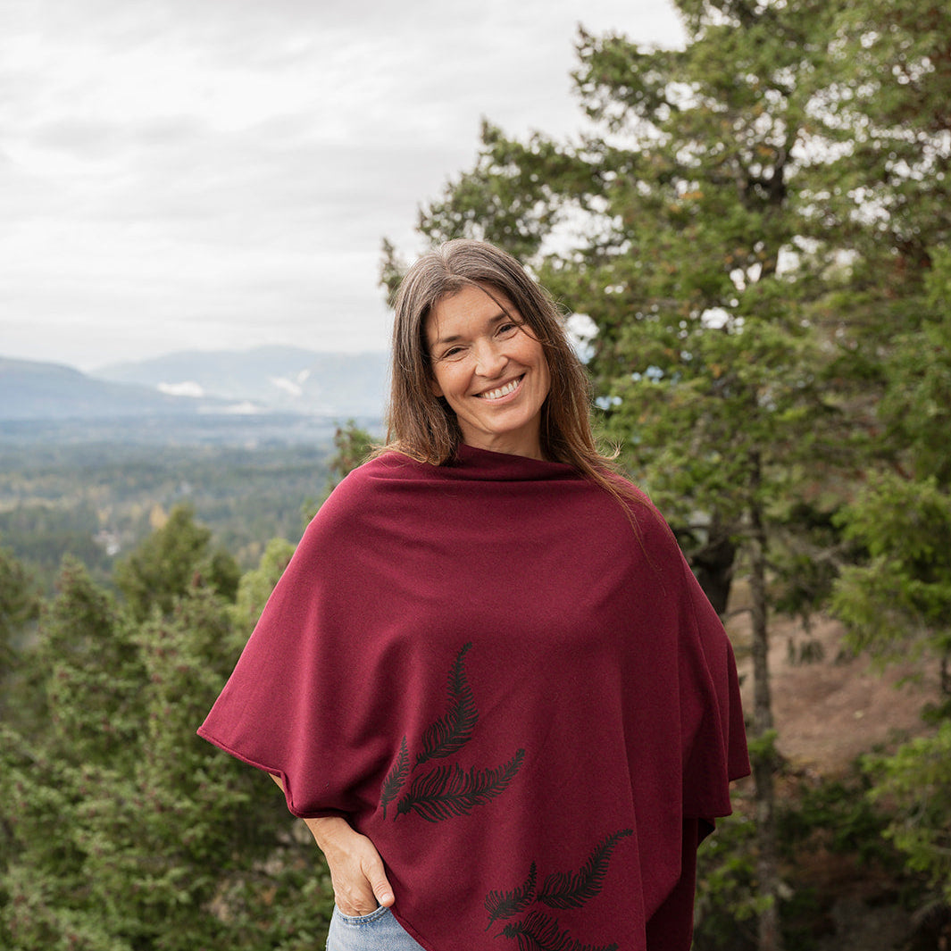 Woman wearing a burgundy poncho with tree designs in a forest setting