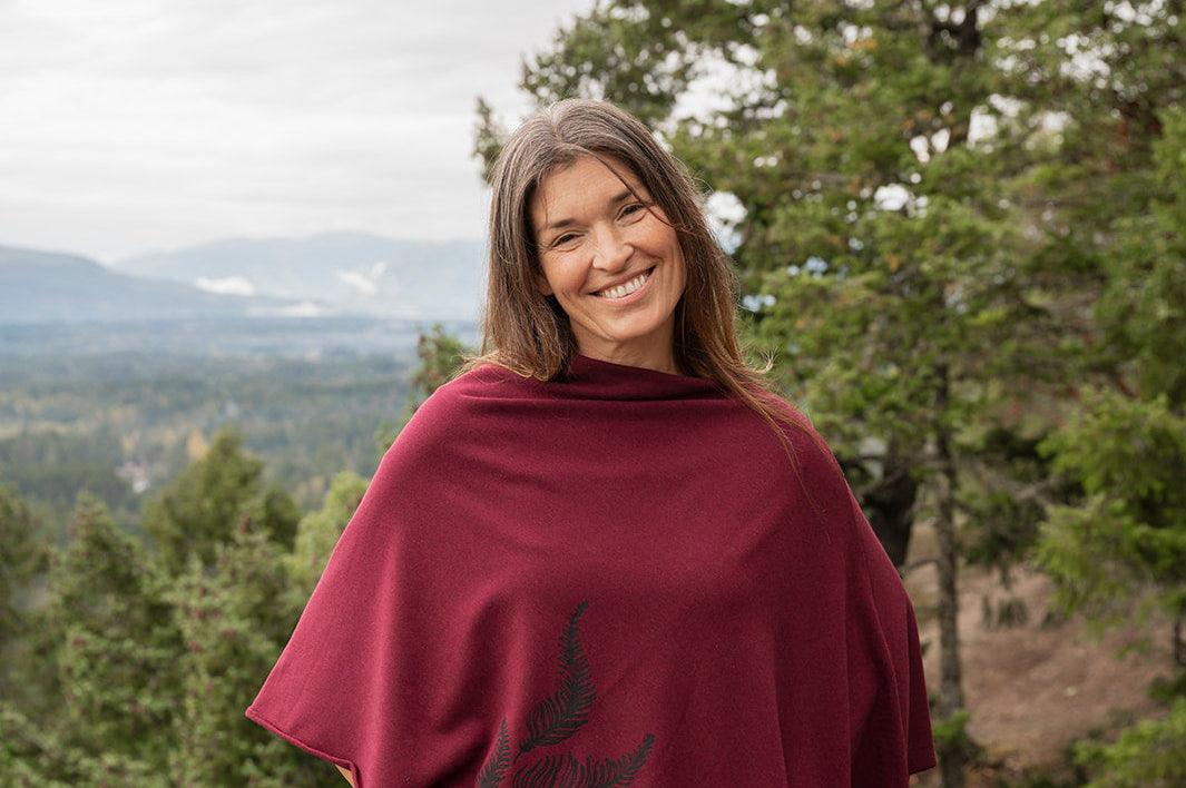 Woman wearing a burgundy poncho with tree designs in a forest setting