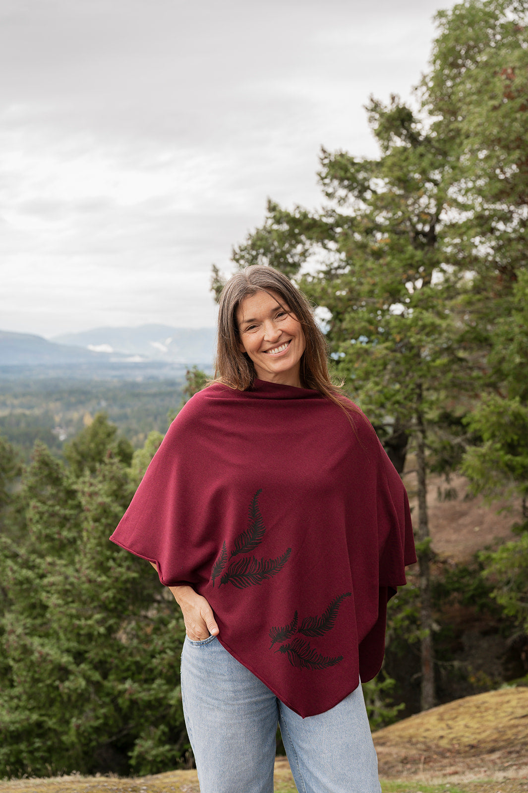 Woman wearing a burgundy poncho with tree designs in a forest setting