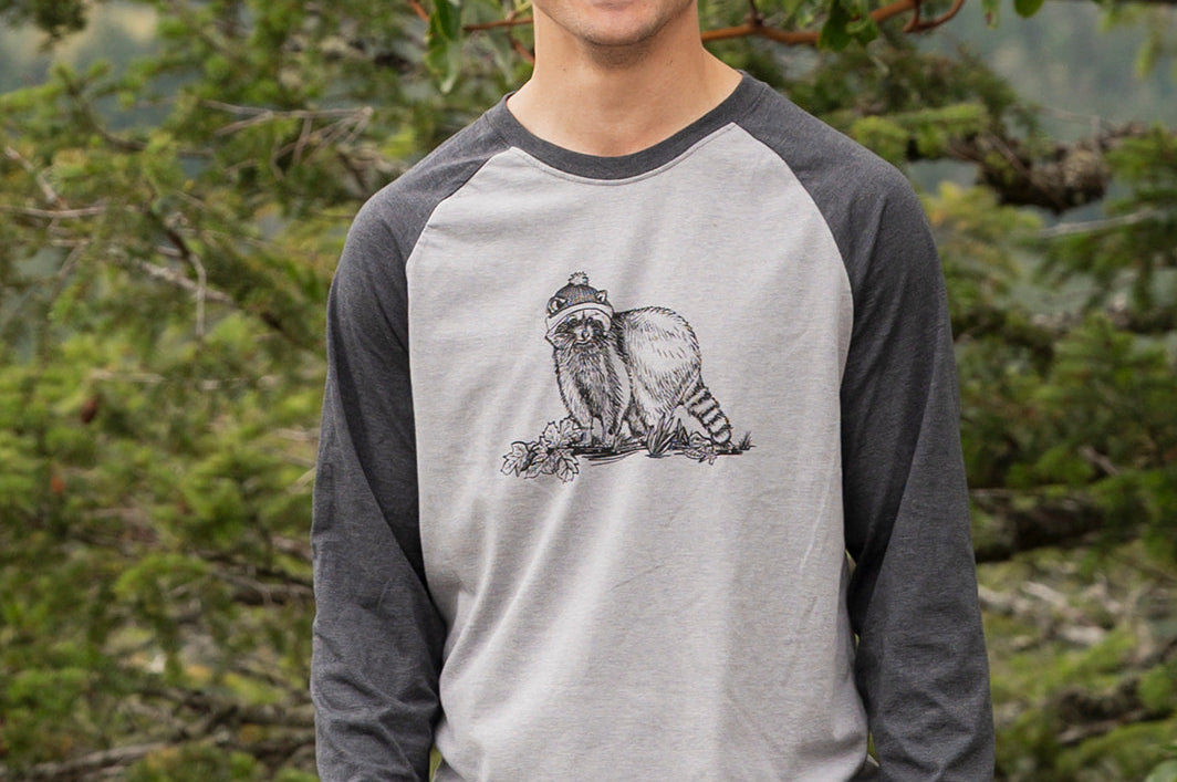 Man wearing a gray and black baseball shirt with a graphic design, standing in a forest.