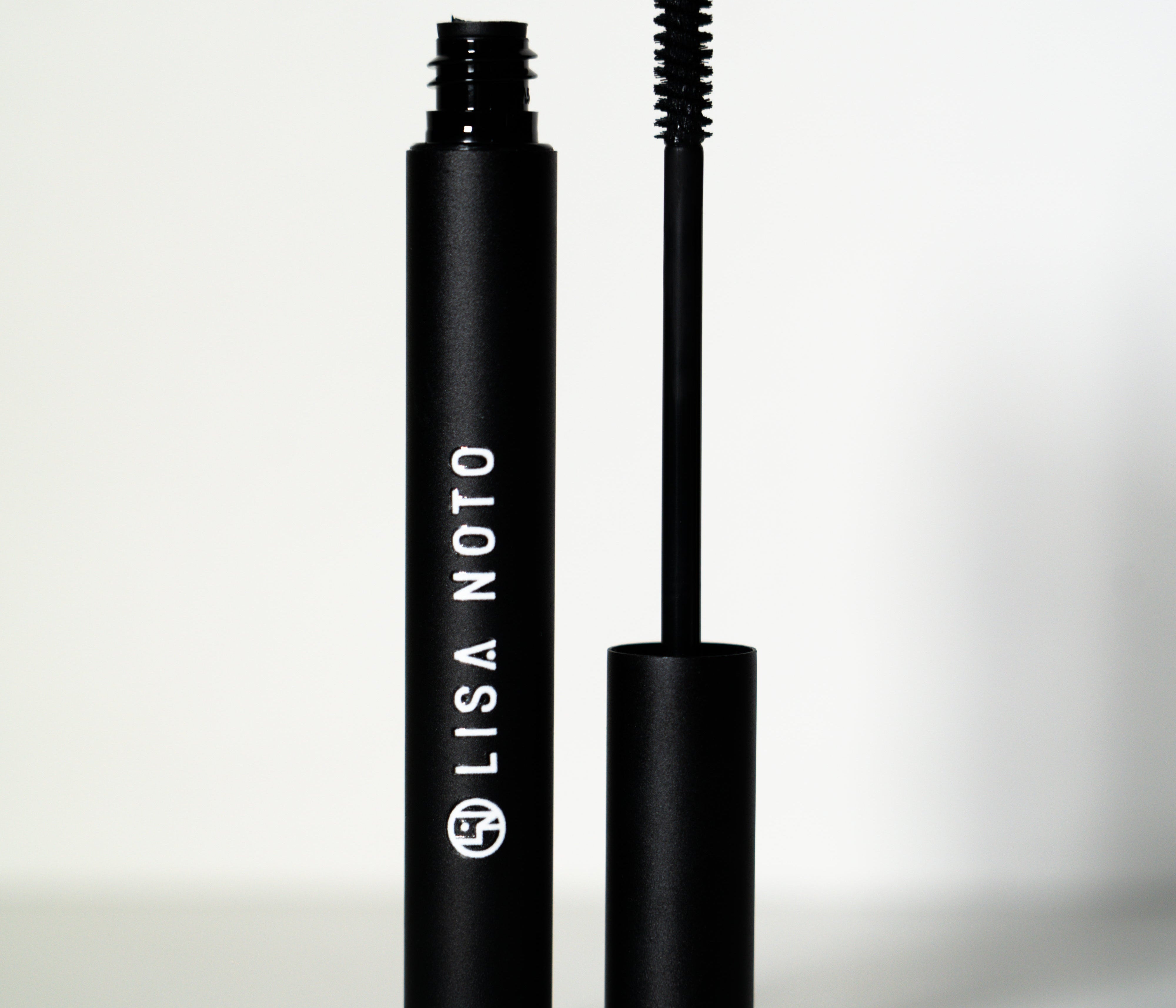 LISA NOTO Volumizing Natural Mascarain a matte black tube, shown with the wand removed and standing beside the cap on a clean white background.