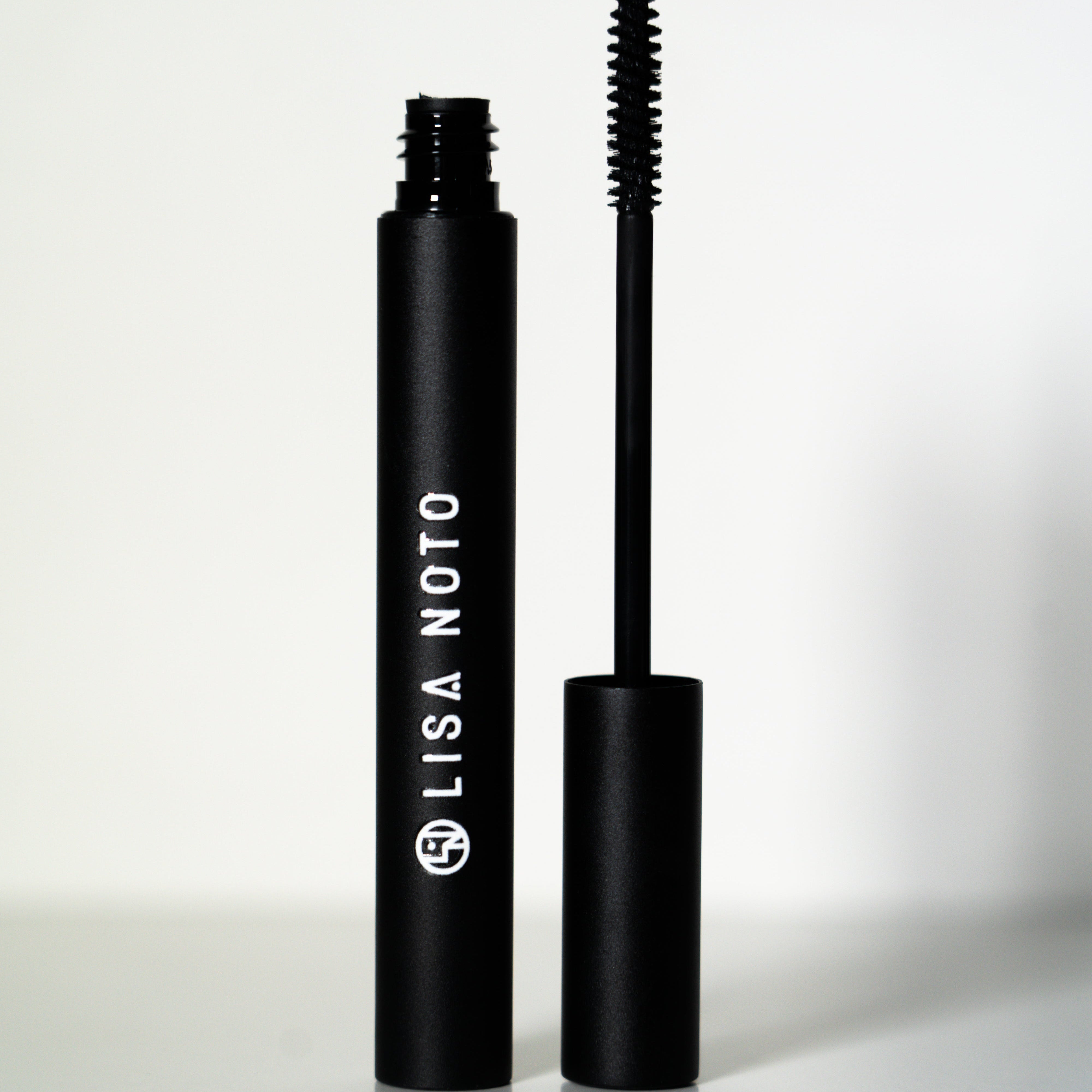 LISA NOTO Volumizing Natural Mascarain a matte black tube, shown with the wand removed and standing beside the cap on a clean white background.