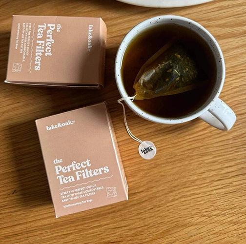 Two boxes of 'lake&Oak' tea filters next to a cup of tea on a wooden surface.