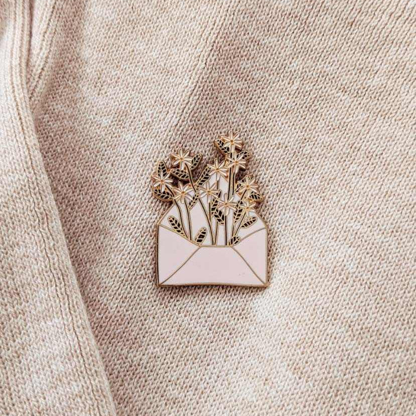 Enamel pin of a bouquet in an envelope on a beige fabric background mimi-and-august