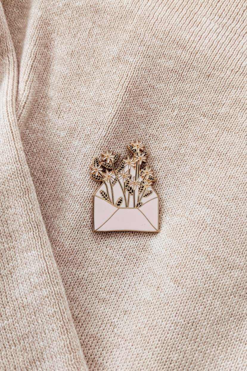 Enamel pin of a bouquet in an envelope on a beige fabric background mimi-and-august