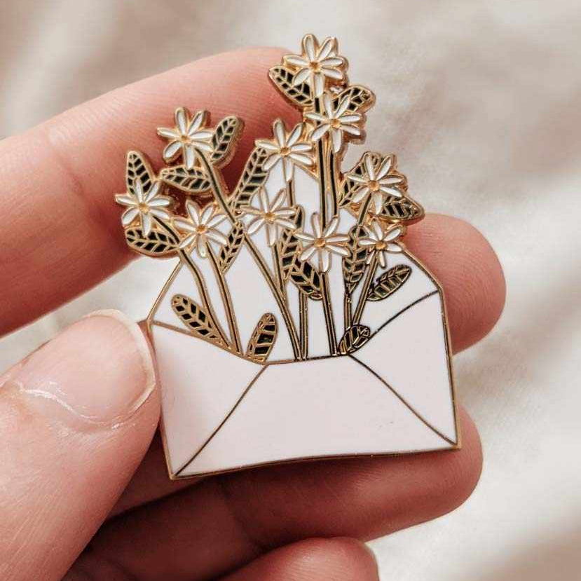 Pin with floral design held between fingers against a neutral background mimi-and-august
