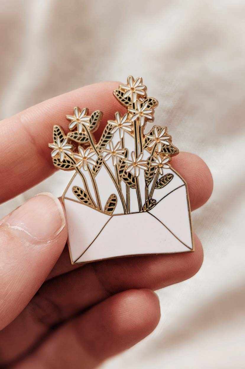 Pin with floral design held between fingers against a neutral background mimi-and-august