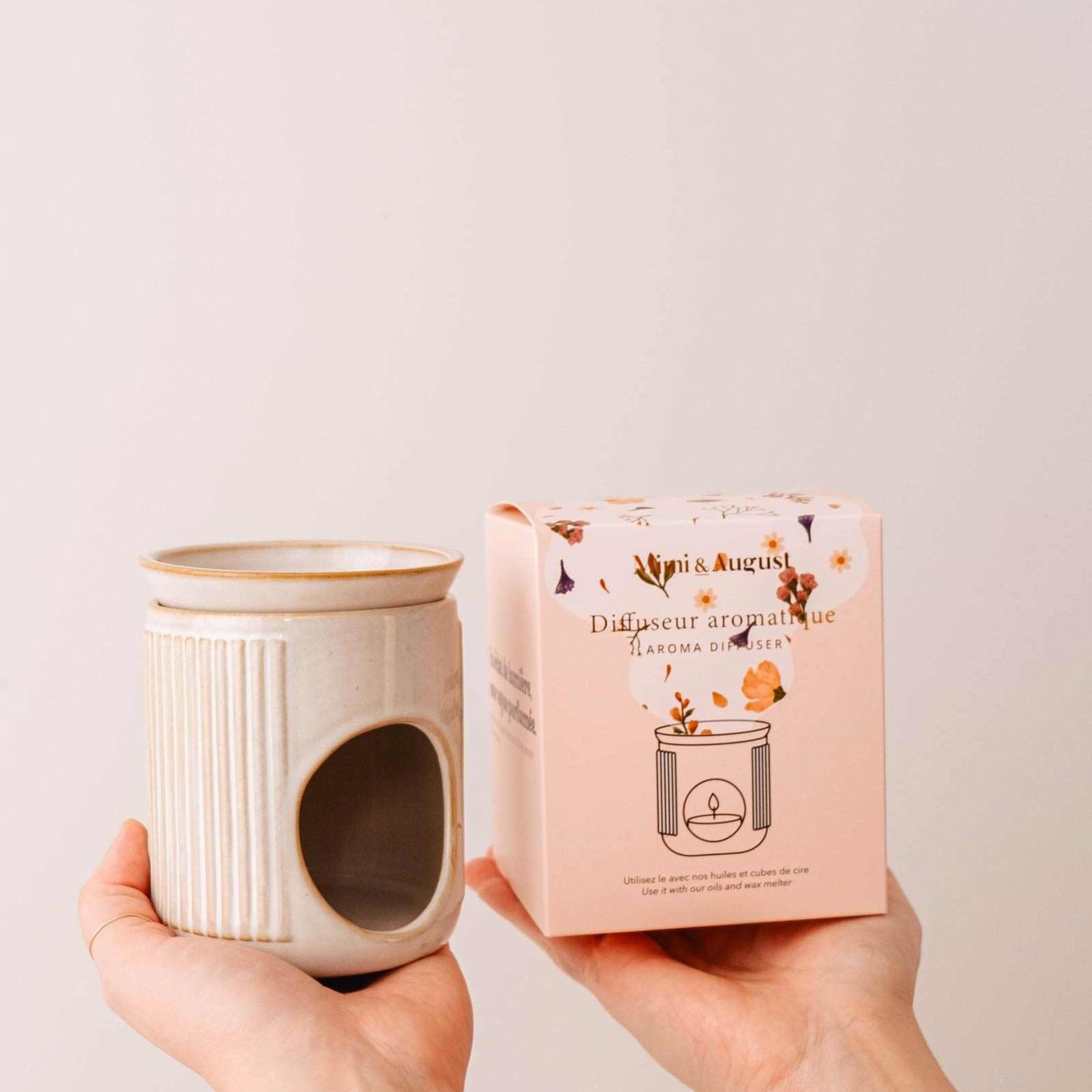Person holding Mimi and August ceramic diffuser and its packaging with a plain background