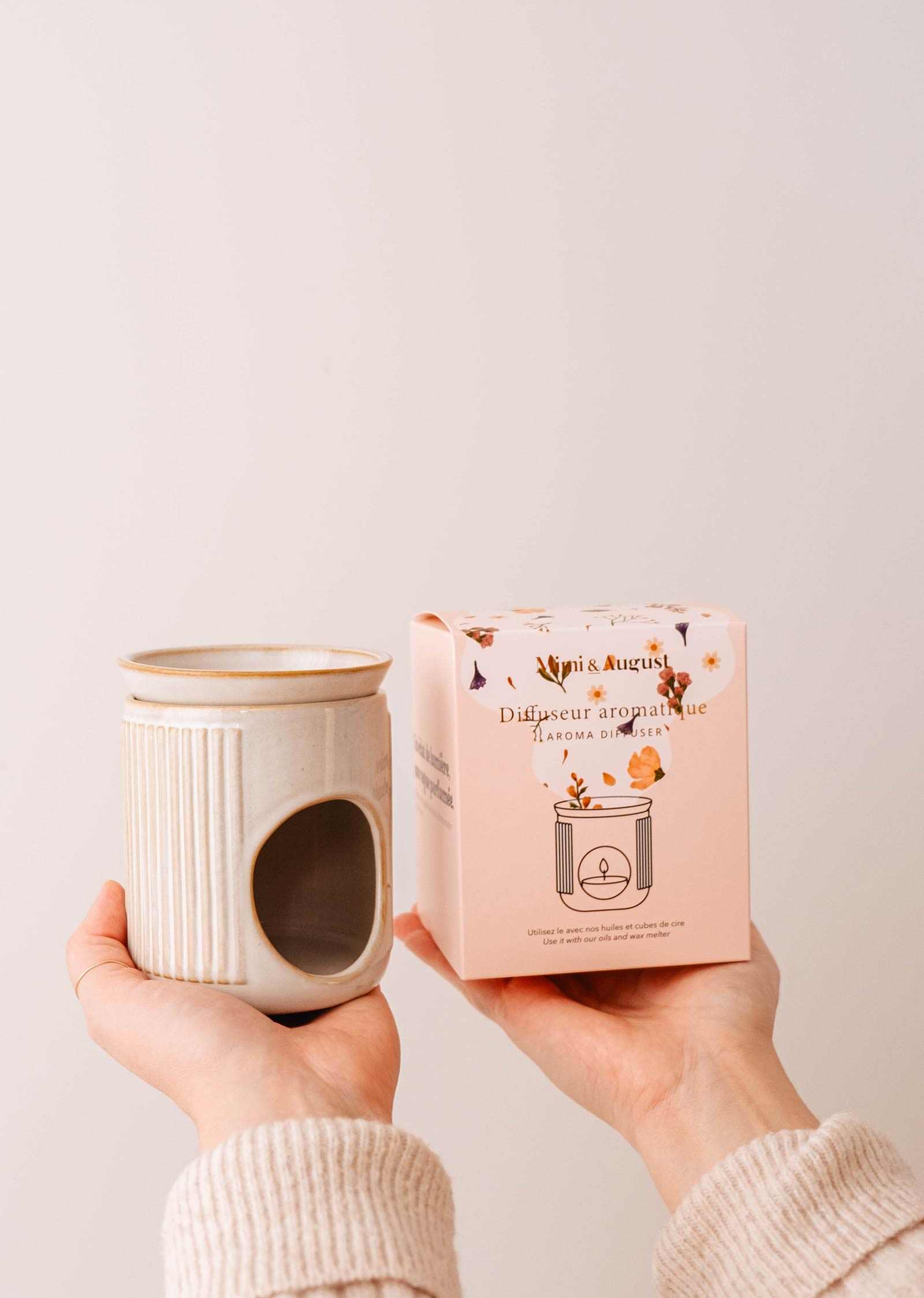 Person holding Mimi and August ceramic diffuser and its packaging with a plain background