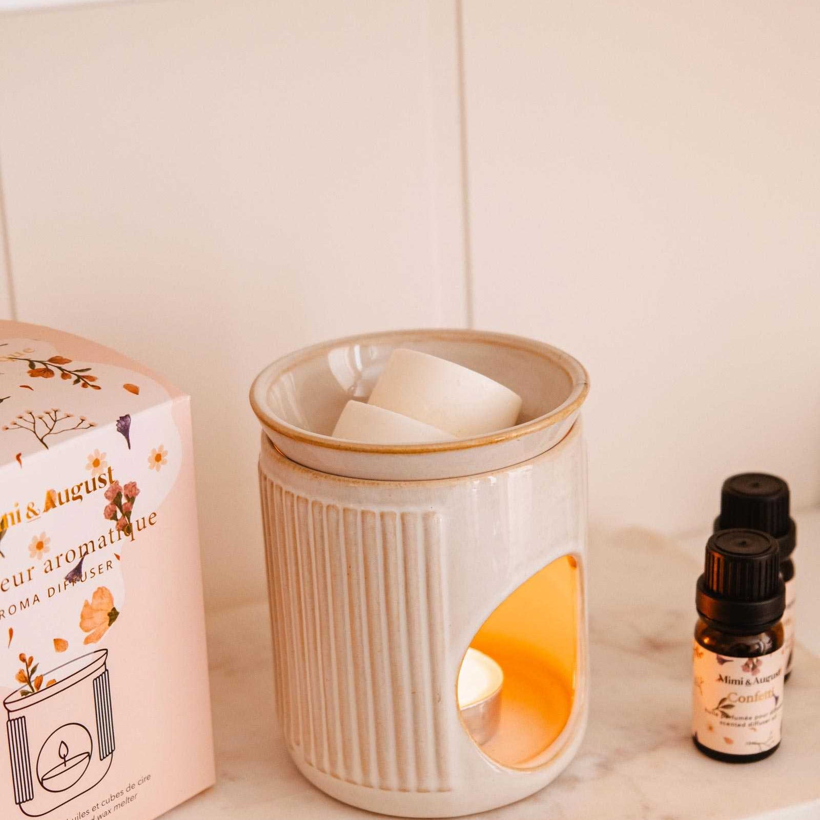 Mimi and August ceramic diffuser a lit candle, packaging, and essential oil bottle on a shelf.