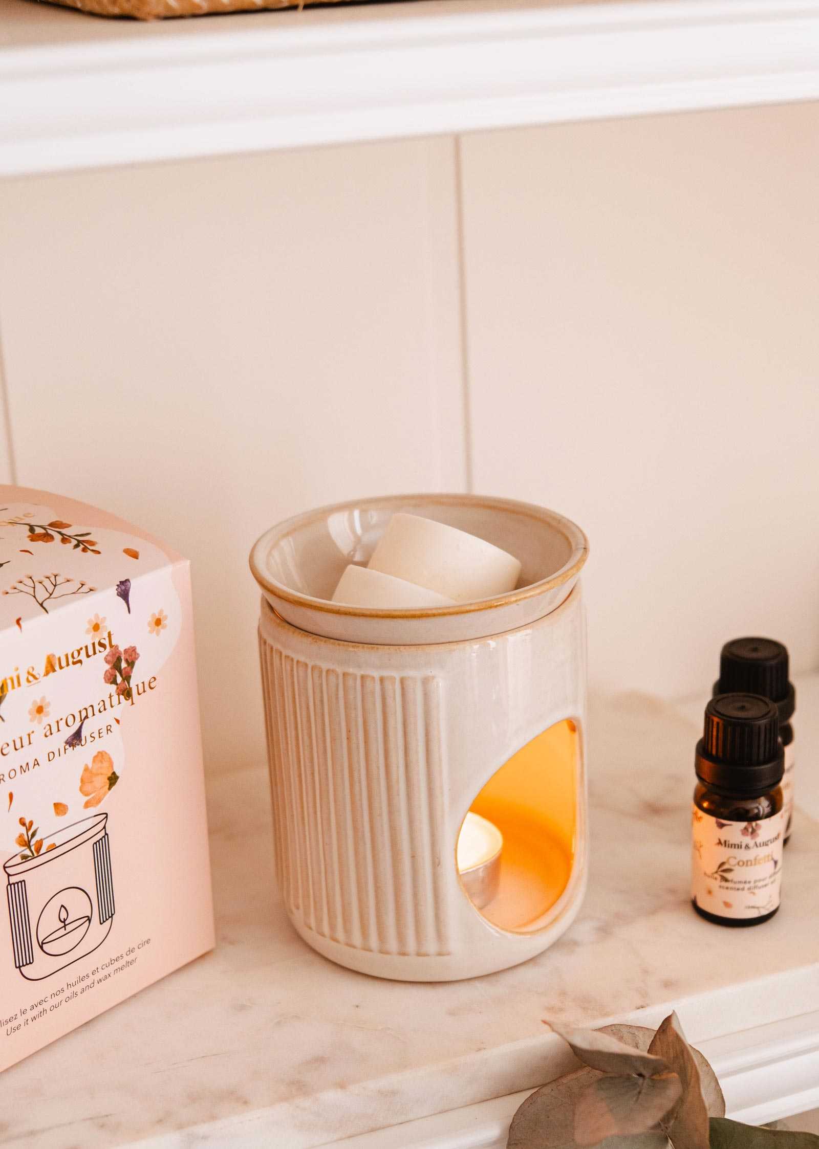 Mimi and August ceramic diffuser a lit candle, packaging, and essential oil bottle on a shelf.
