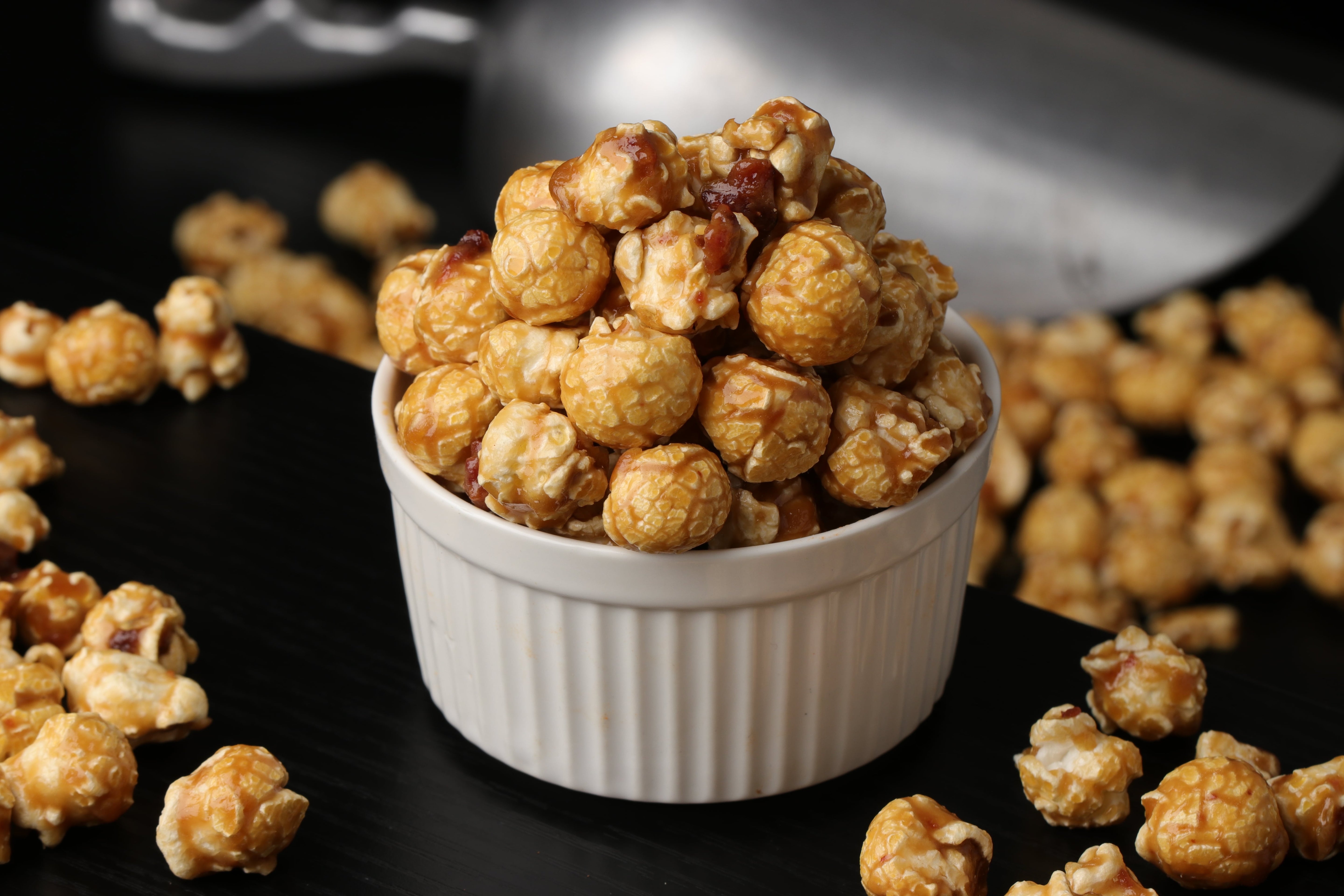 white Bowl of candied maple bacon popcorn on a wooden surface from Toronto Popcorn company