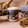 Candle with 'Mimi & August Mare' packaging on a textured surface with driftwood.