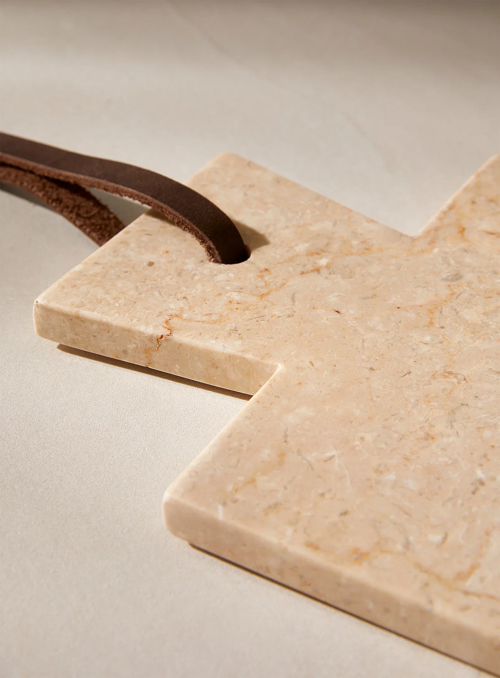Marble & Teak Cutting Board with leather handle on a beige background