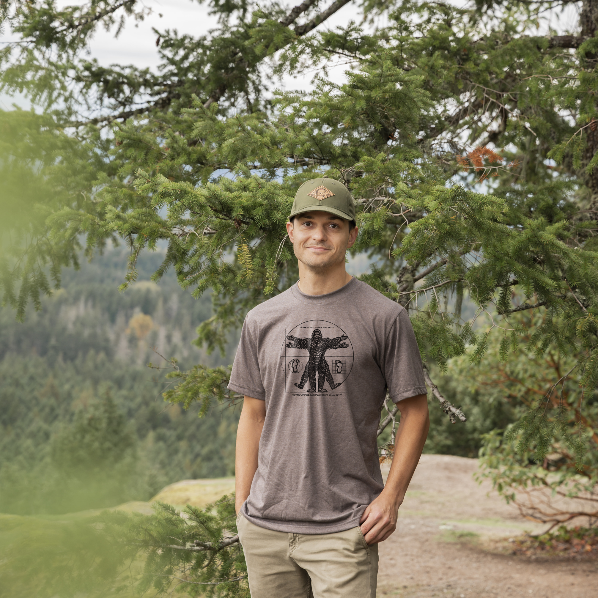 Man standing in a forested area wearing a cap and t-shirt.