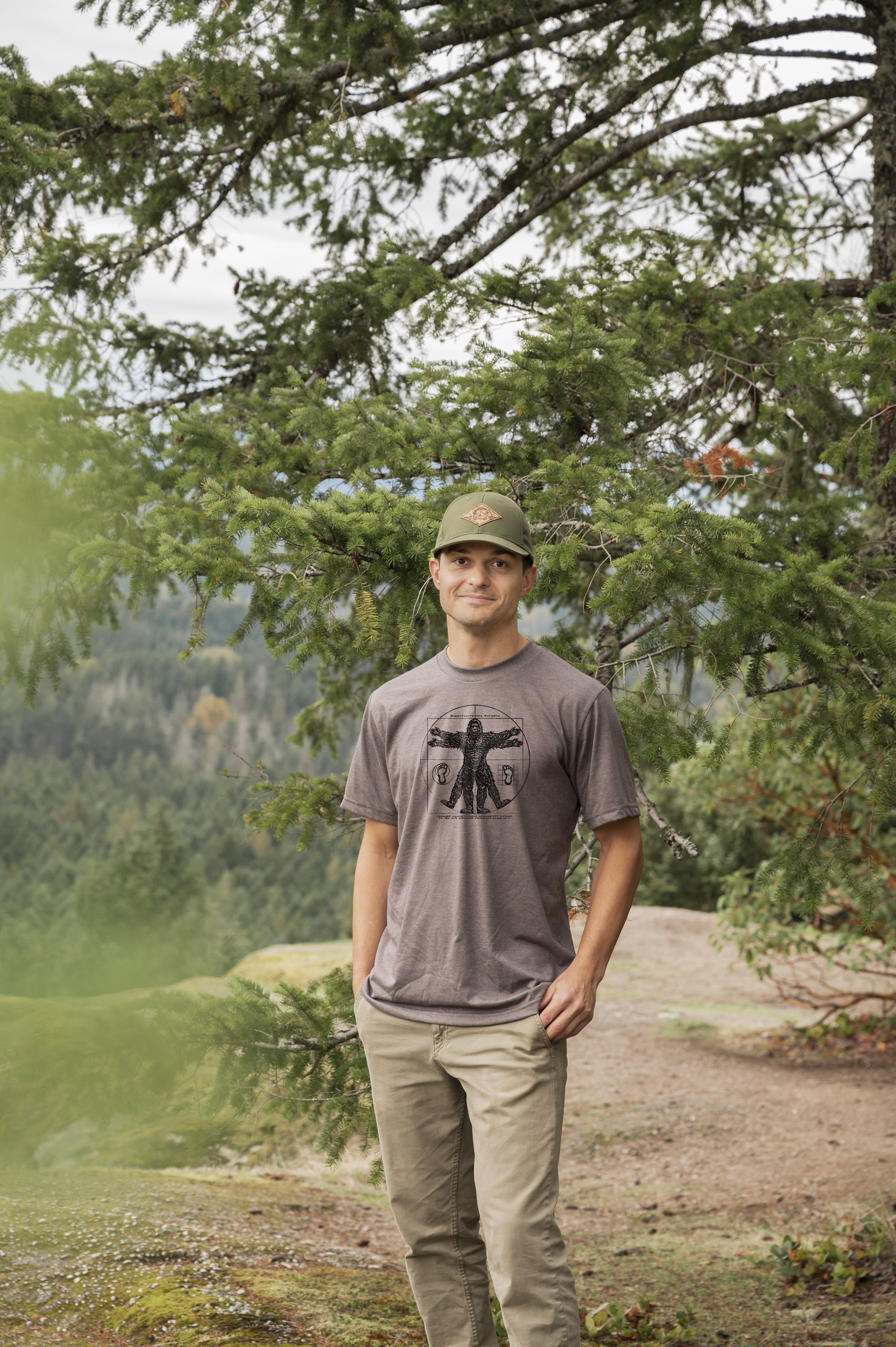 Man standing in a forested area wearing a cap and t-shirt.