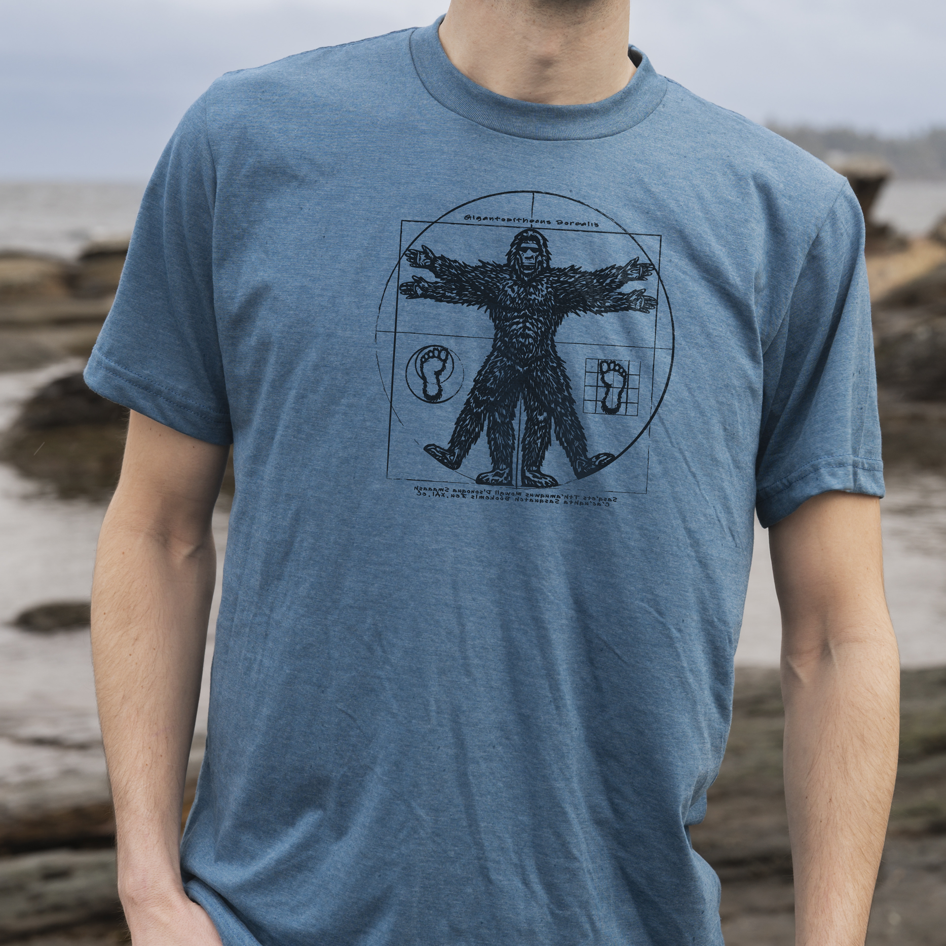 Man wearing a blue t-shirt with a graphic design standing on a beach.
