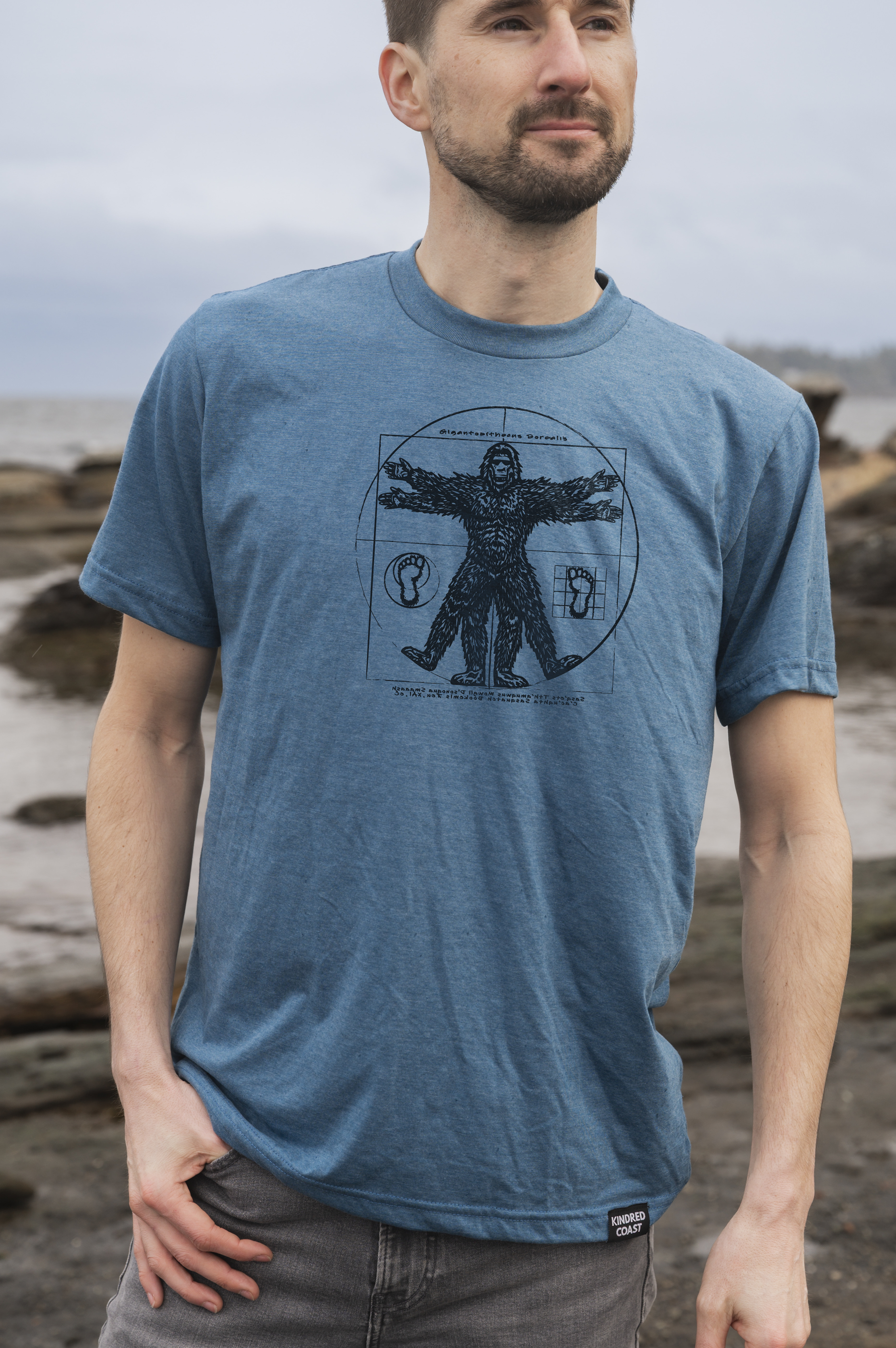 Man wearing a blue t-shirt with a graphic design standing on a beach.