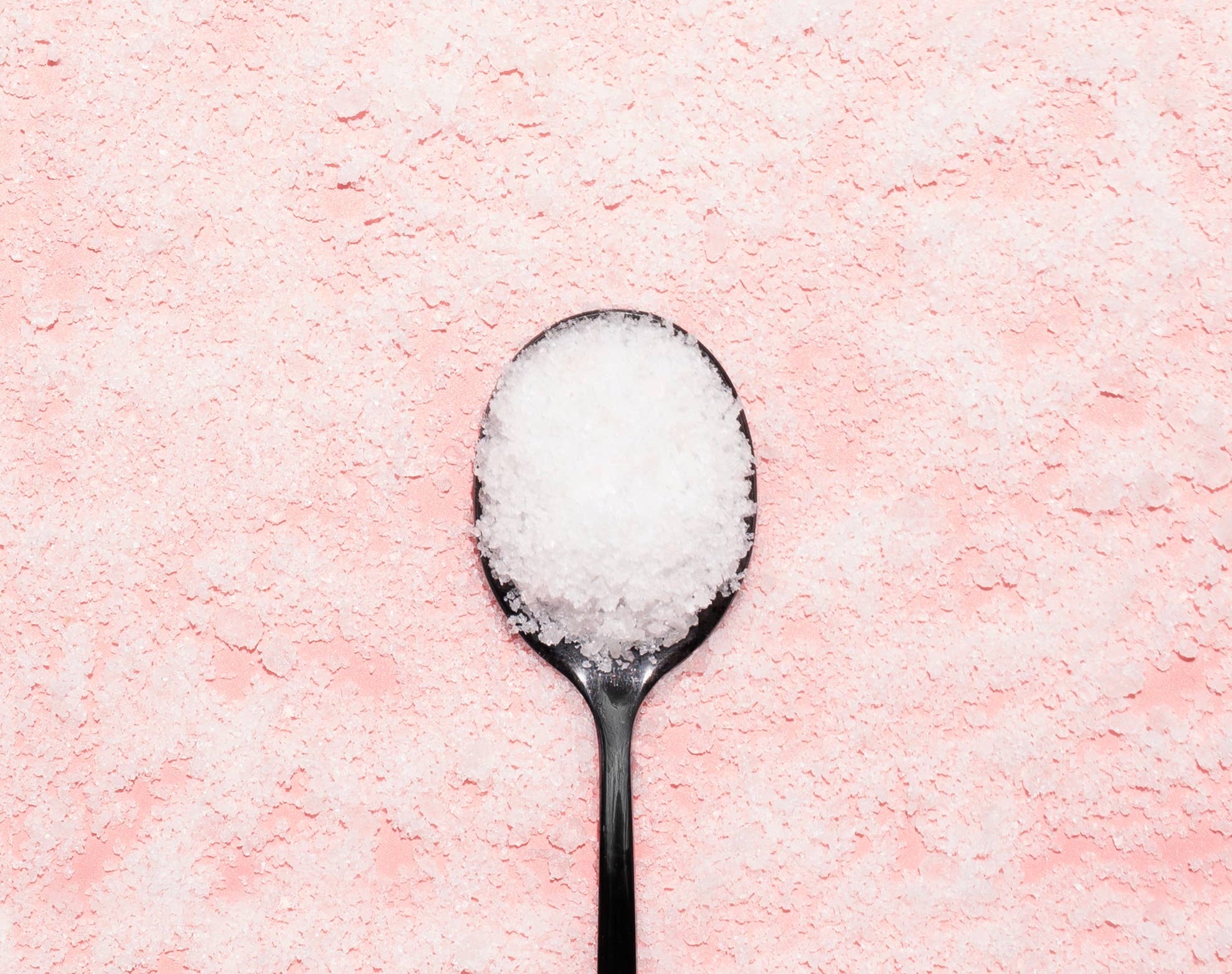  spoon filled with white Epsom salt on a pink background, perfect for bath soak products like Bing Cherries + Clove.