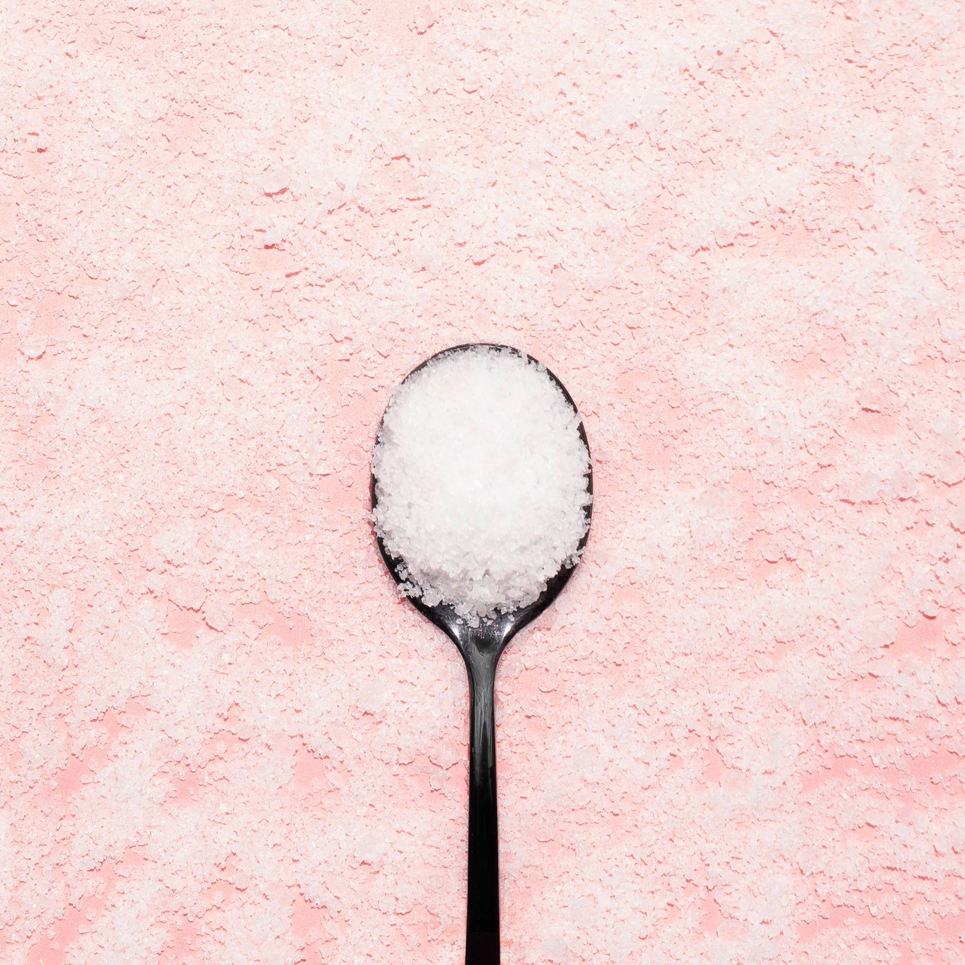  spoon filled with white Epsom salt on a pink background, perfect for bath soak products like Bing Cherries + Clove.