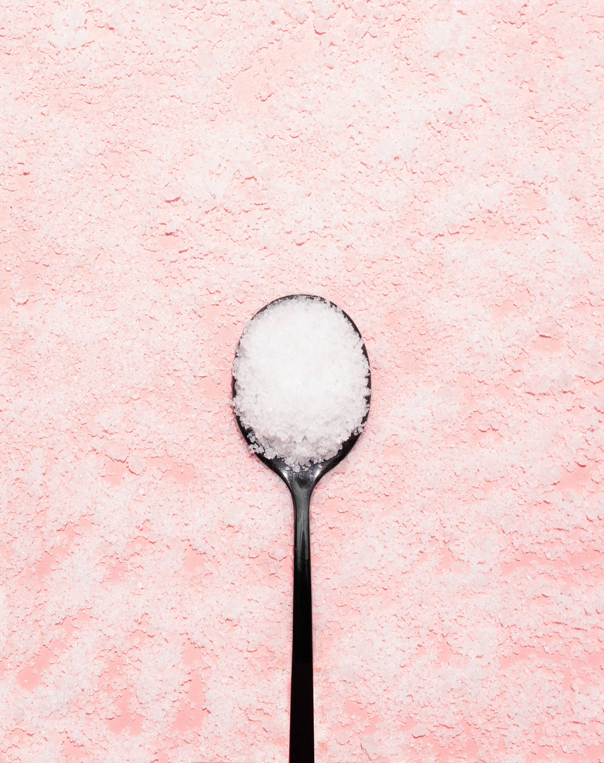  spoon filled with white Epsom salt on a pink background, perfect for bath soak products like Bing Cherries + Clove.