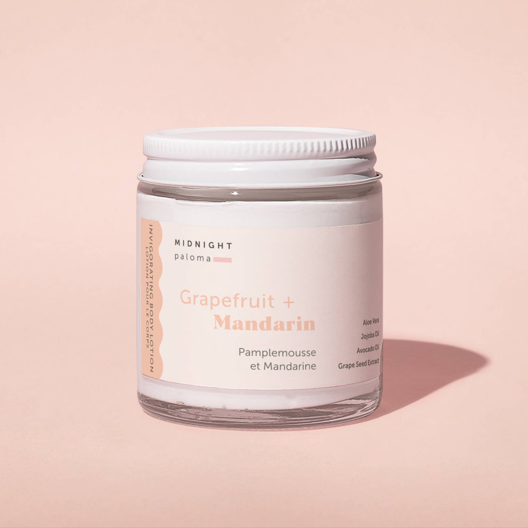 Grapefruit + Mandarin Body Lotion 4 oz jar on pink background, hydrating formula with tropical scent by Midnight Paloma