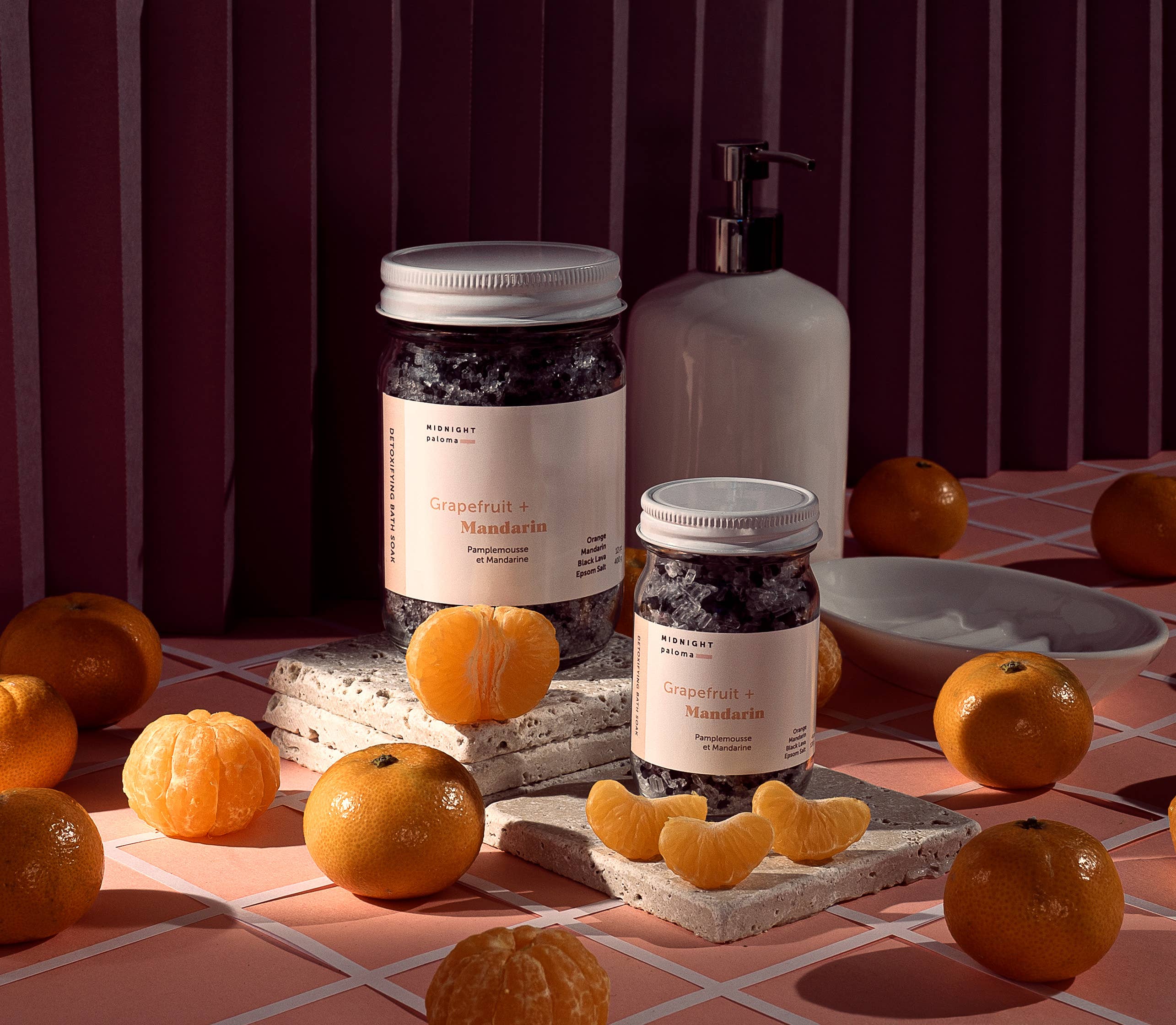 Midnight Paloma Grapefruit + Mandarin detoxifying bath soak products surrounded by fresh mandarins on a stylish surface.