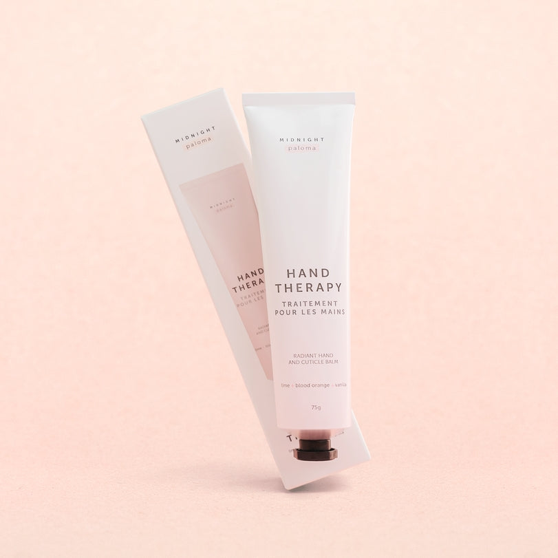 Hand Therapy Cream tube with packaging on a soft pink background, enriched with Blood Orange and Grapefruit scents.