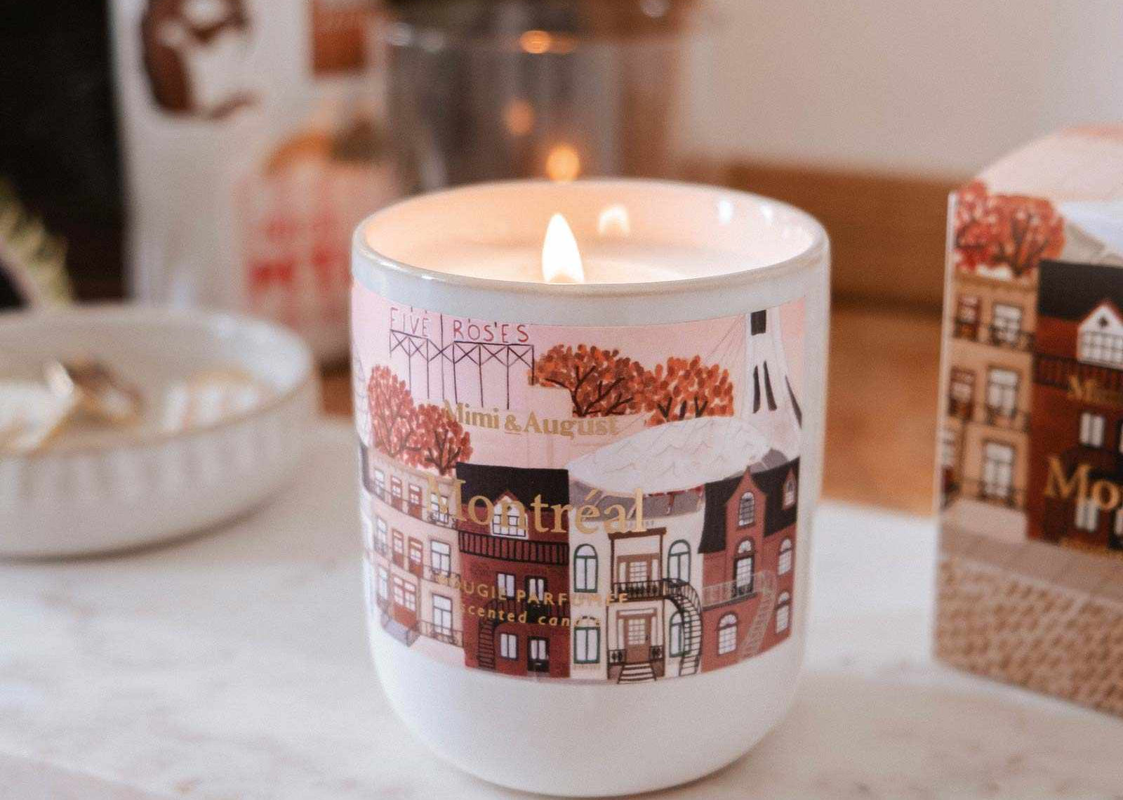 Candle in a decorative mug with a town design on a marble surface.