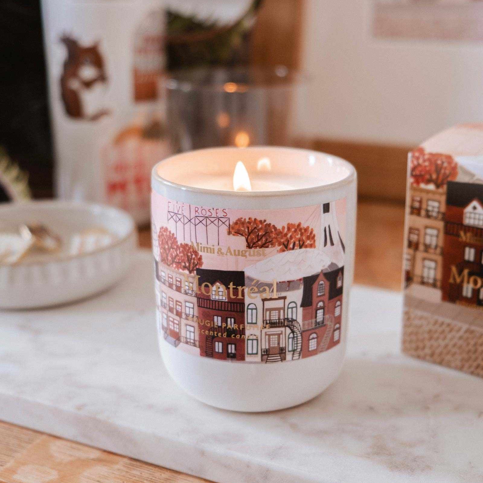 Candle in a decorative mug with a town design on a marble surface.