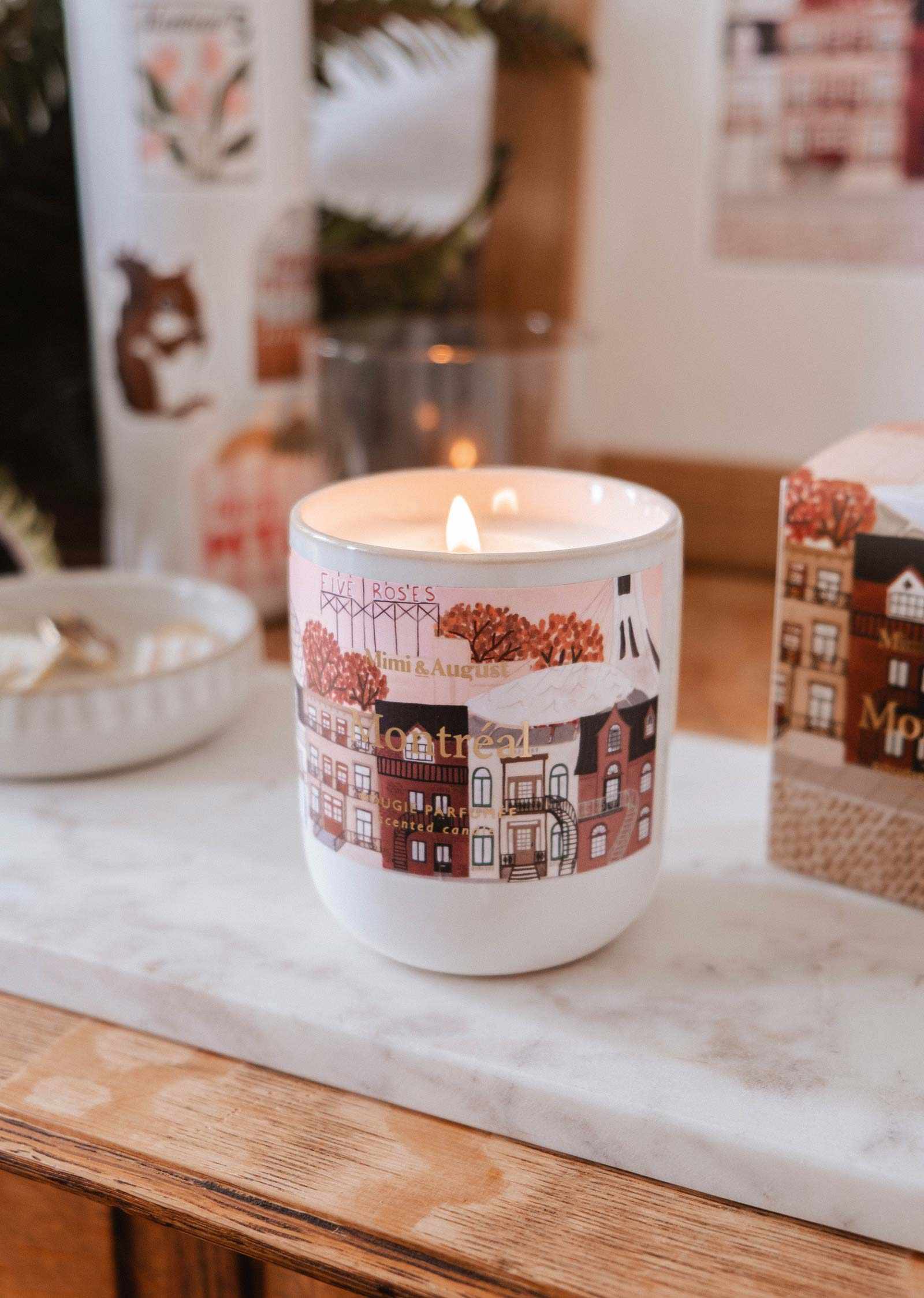 Candle in a decorative mug with a town design on a marble surface.