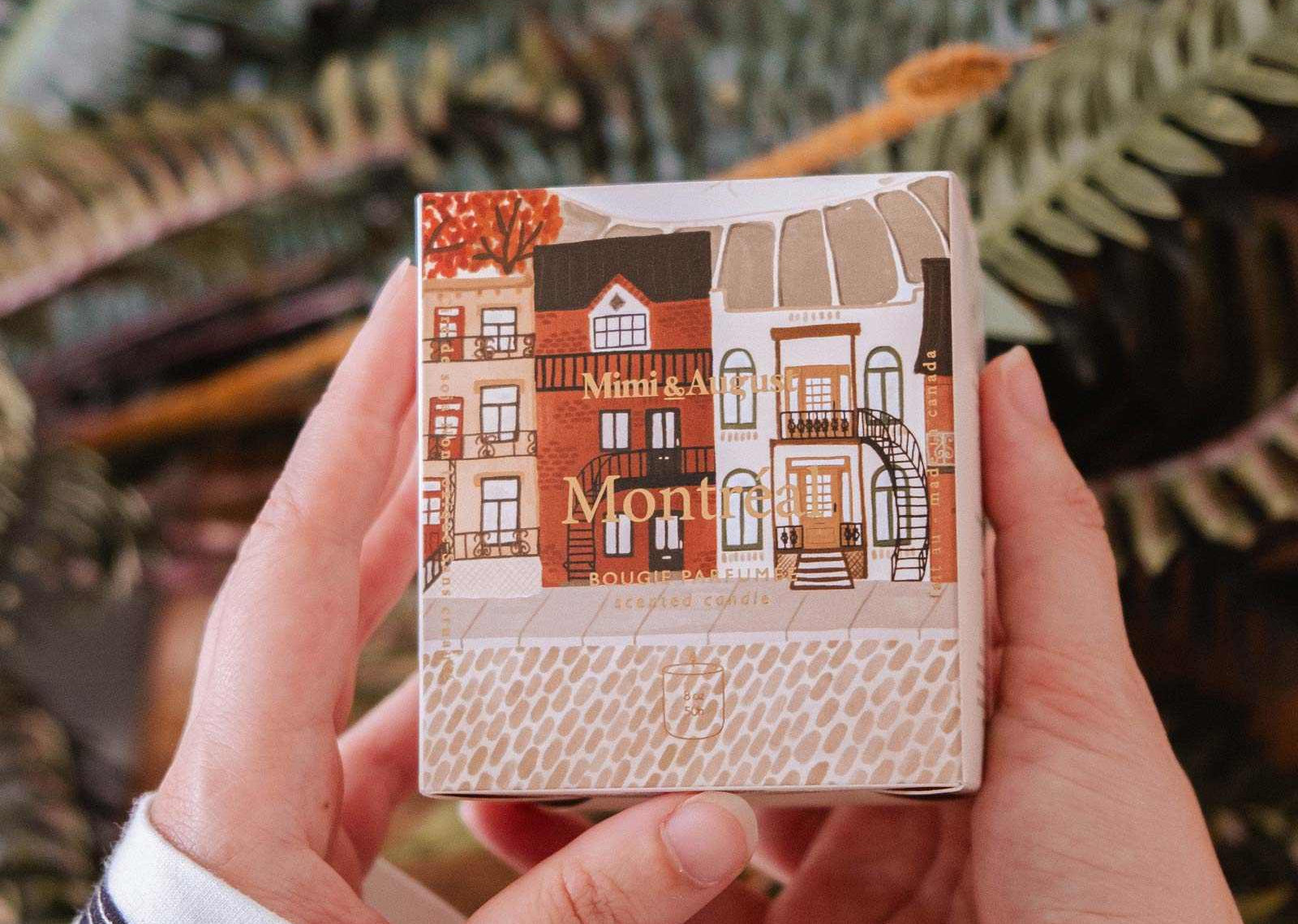 Person holding a small notebook with a cover design of houses and 'Montmartre' text, against a blurred natural background.