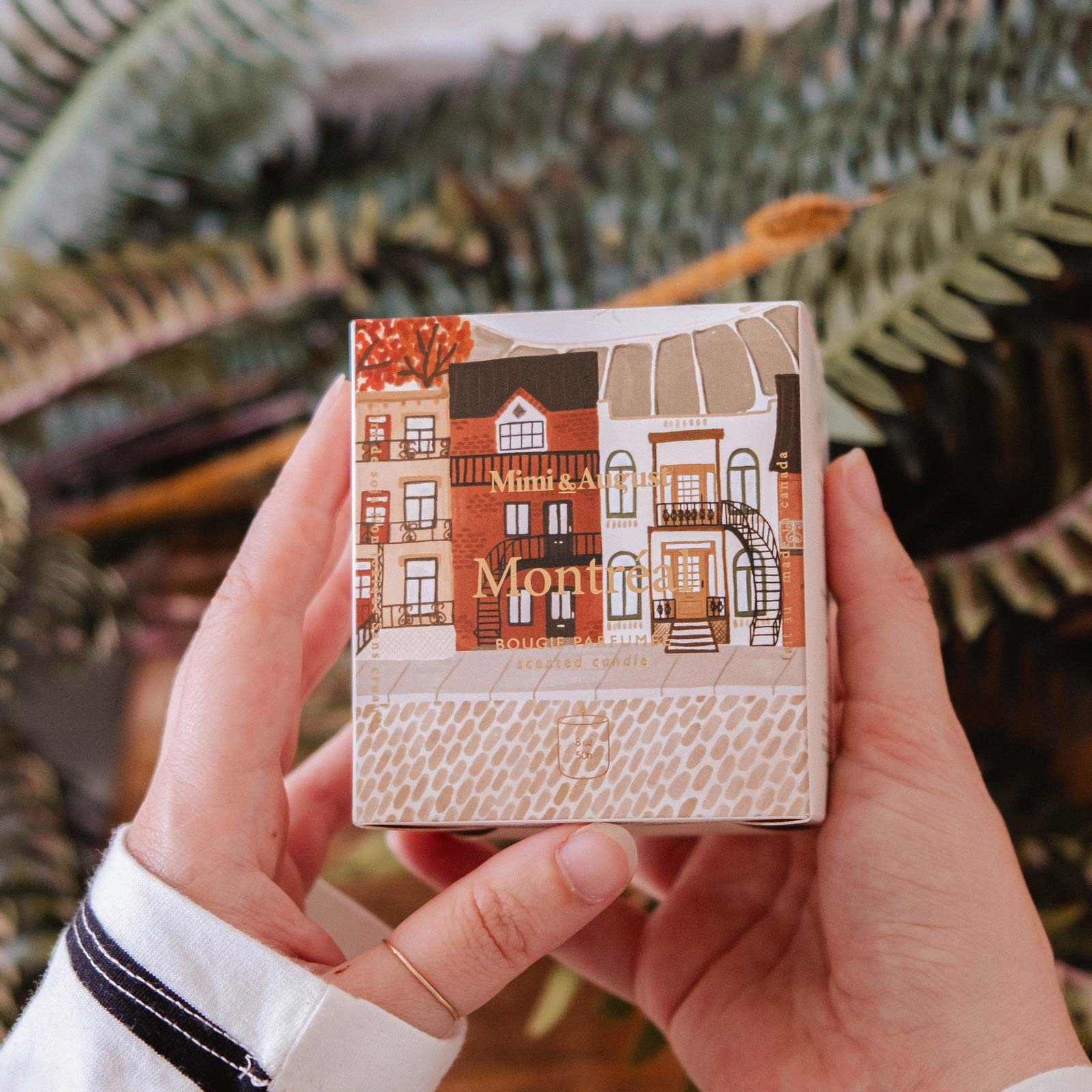Person holding a small notebook with a cover design of houses and 'Montmartre' text, against a blurred natural background.
