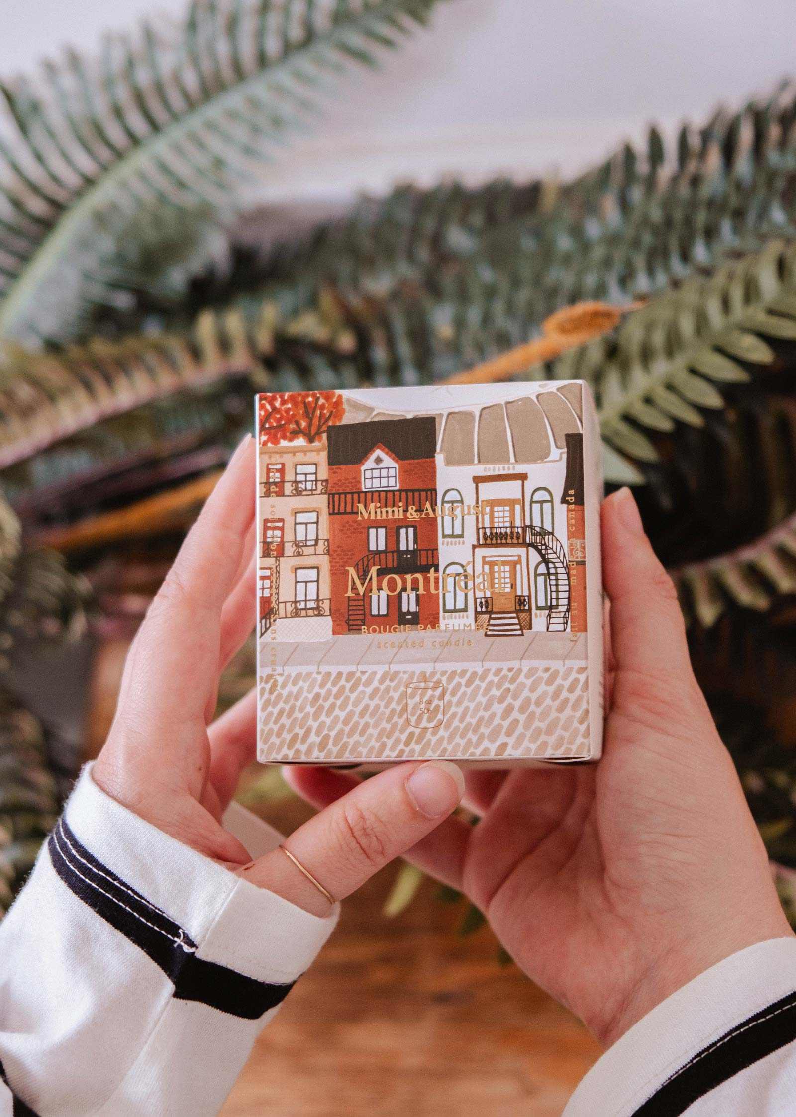 Person holding a small notebook with a cover design of houses and 'Montmartre' text, against a blurred natural background.