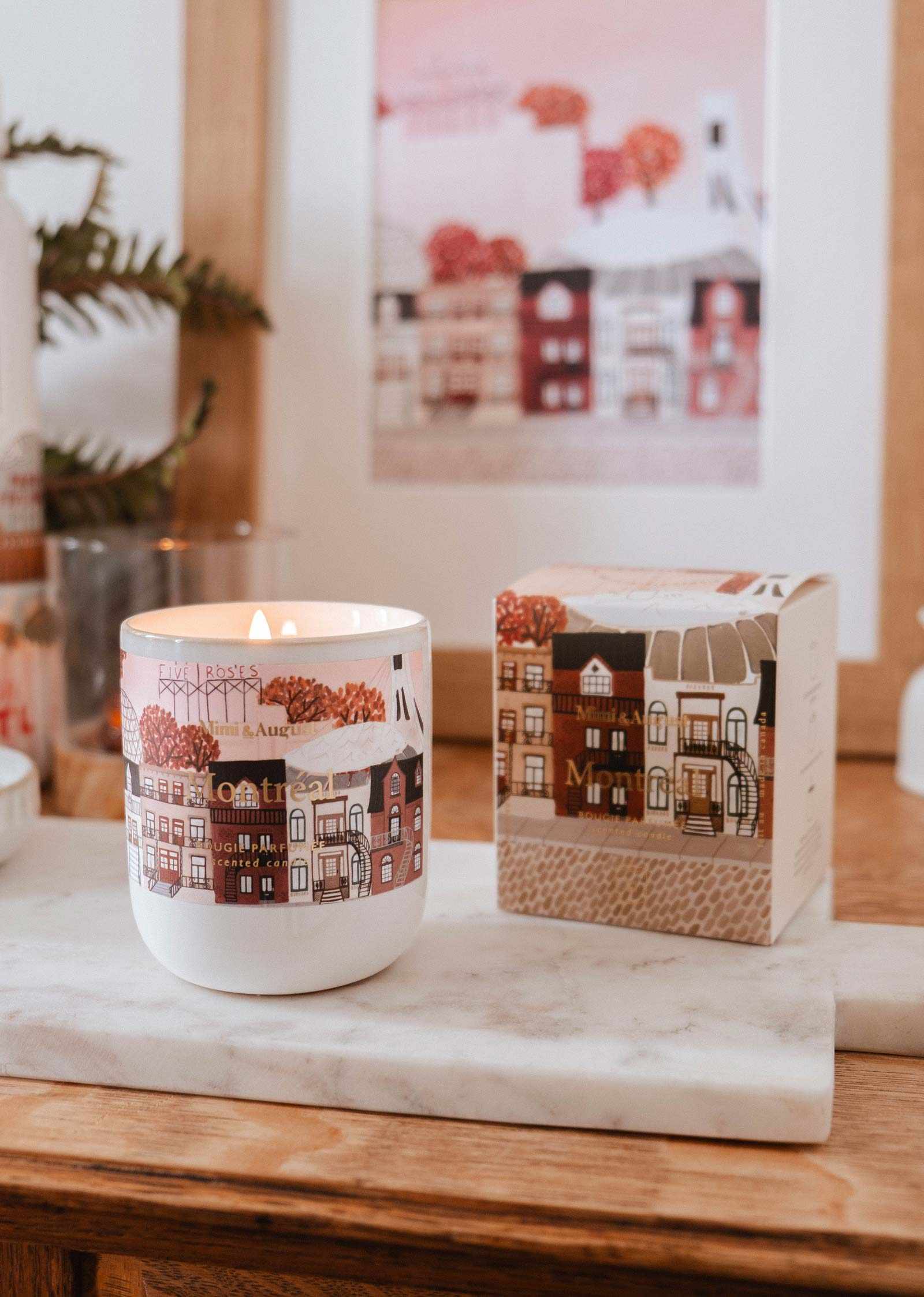 Candle with a decorative design on a marble surface, with a blurred background of a house illustration.