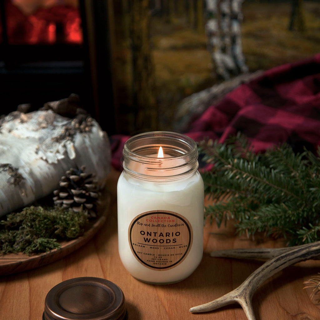 Candle labeled 'Ontario Woods' on a wooden surface with decorative elements. Stop and Smell the Candles