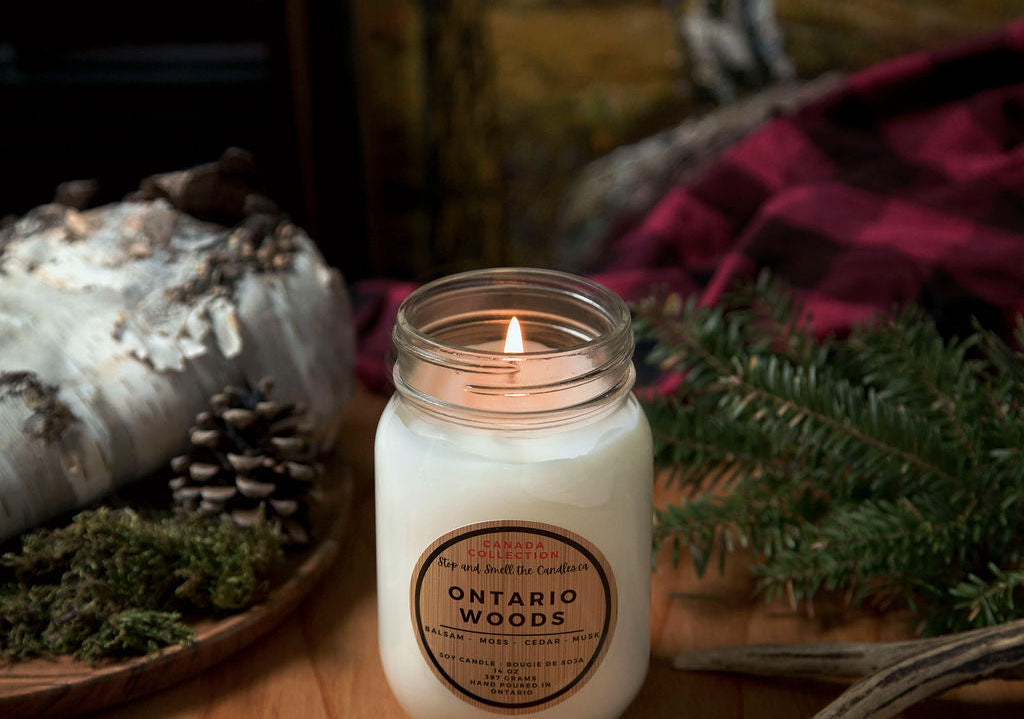 Candle labeled 'Ontario Woods' on a wooden surface with decorative elements. Stop and Smell the Candles