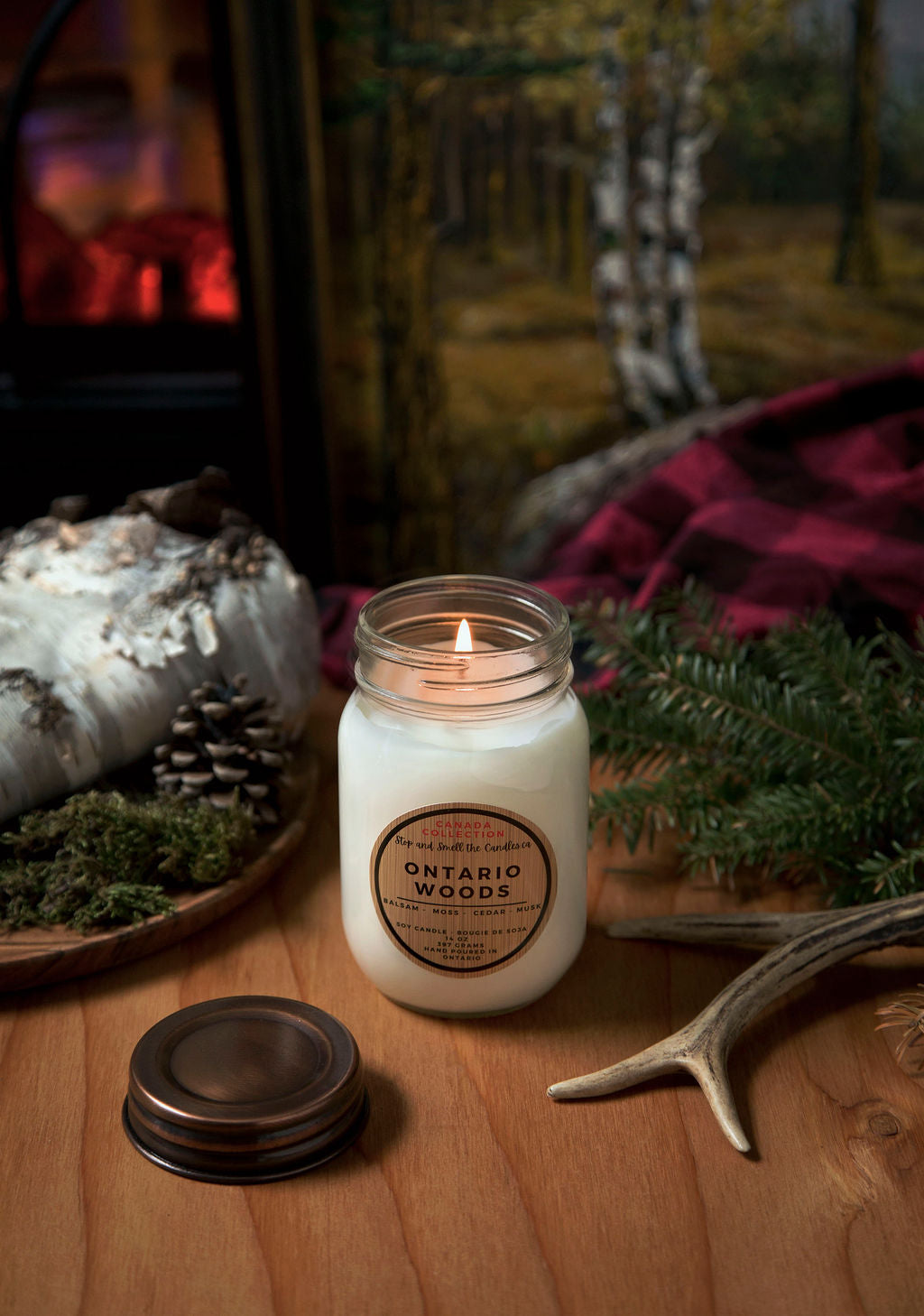 Candle labeled 'Ontario Woods' on a wooden surface with decorative elements. Stop and Smell the Candles