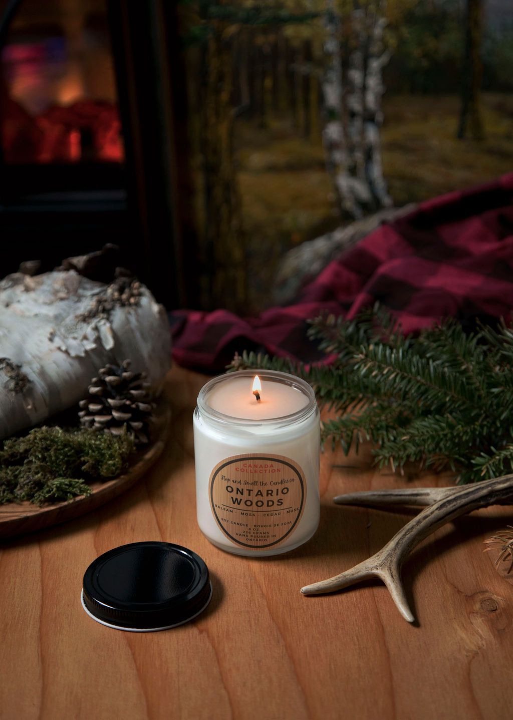 Candle labeled 'Ontario Woods' on a wooden surface with natural elements