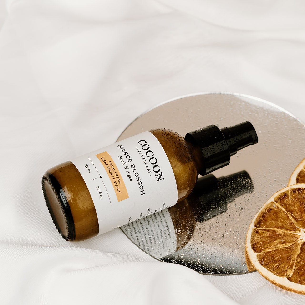 COCOON bottle with a dropper on a reflective surface with dried oranges.