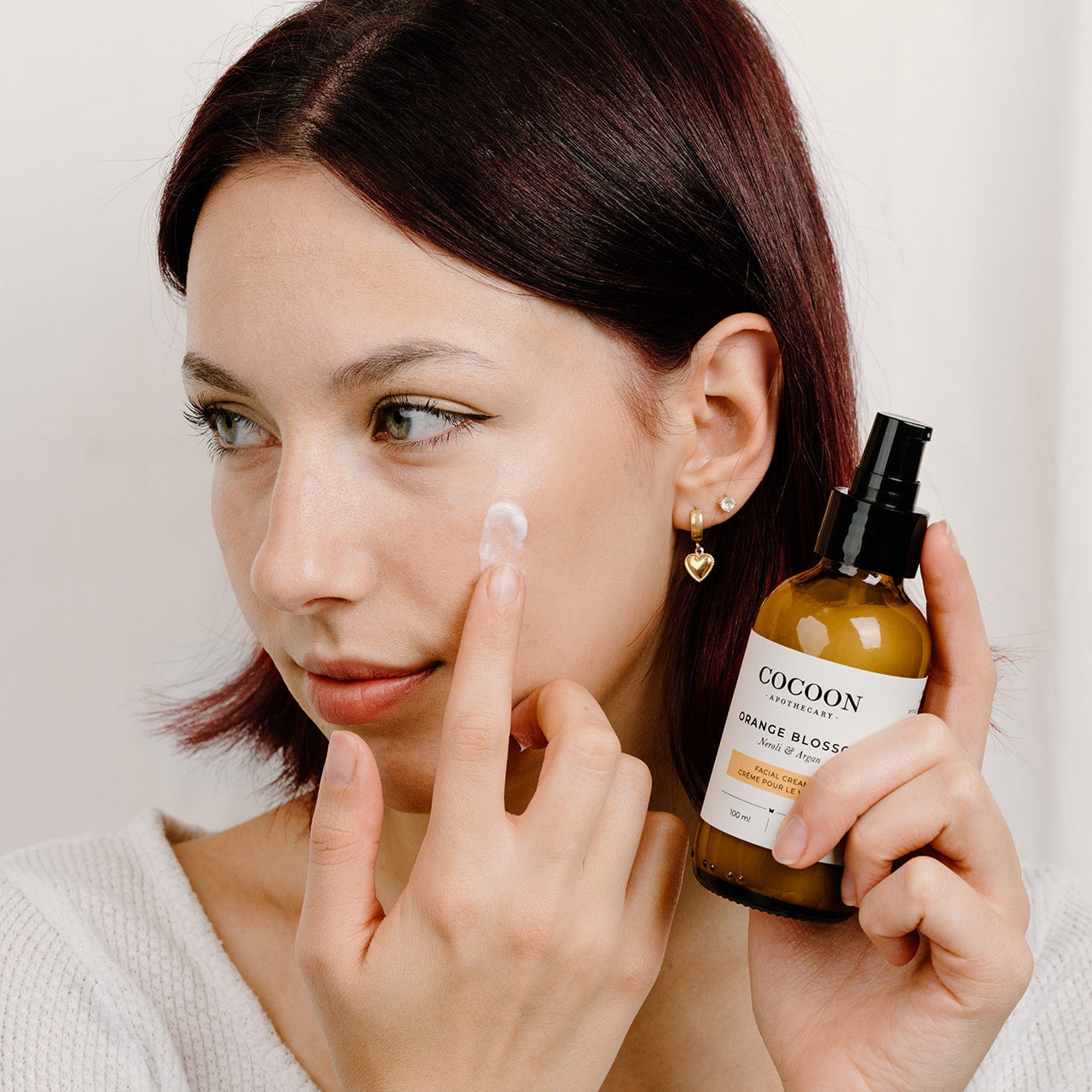 Woman applying a product to her face with a bottle labeled 'Cocoon' in the other hand.