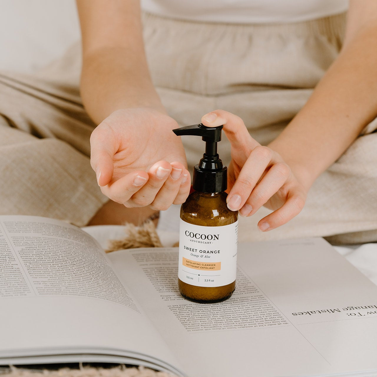 Person holding a bottle of Cocoon Sweet Orange hand cream on an open book.