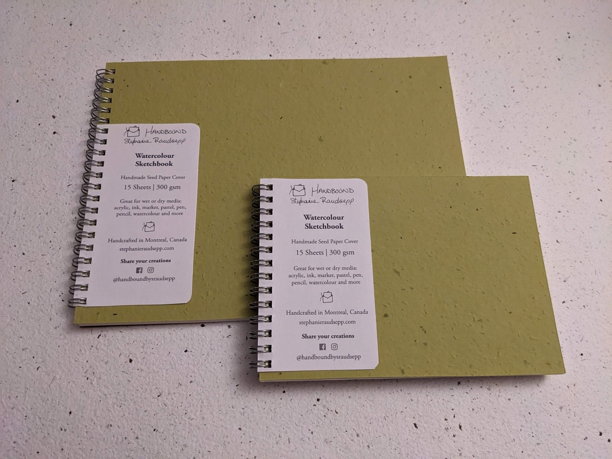 Two green notebooks with spiral binding on a light Large Plantable Watercolour Sketchbook by Creative Artifacts HQ